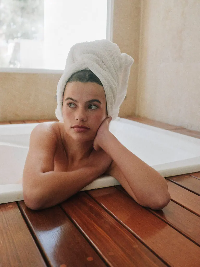 woman in bathroom doing self-care with towel wrapped around her hair