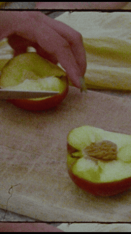 Hand with knife slicing peaches on wooden cutting board